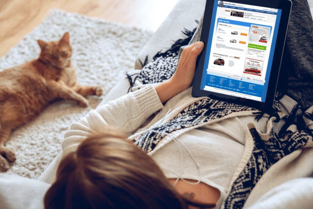 A woman lying on her back, looking at an ipad. A cat sits nearby.
