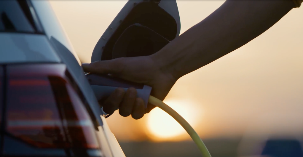 A closeup image of a hand placing the gas nozzle in a car's tank.