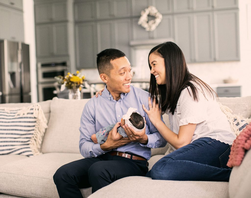 A couple sitting on their couch with their baby.