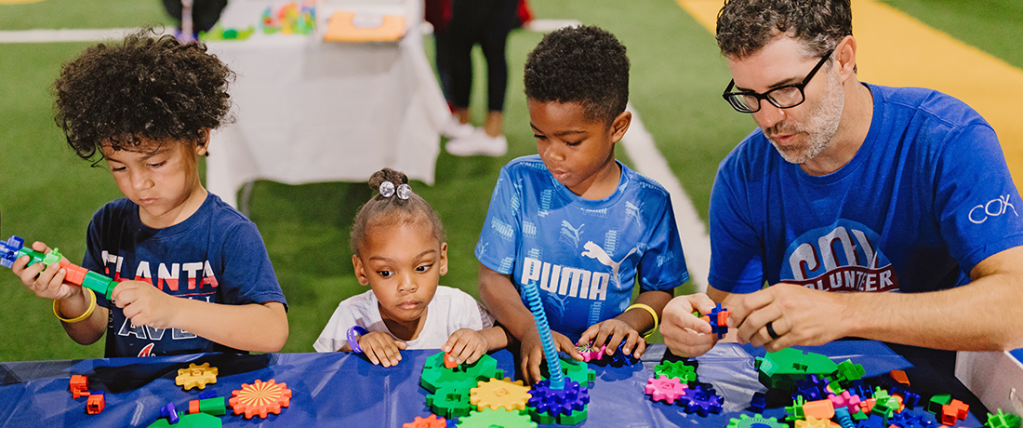 Group of young children and Cox volunteer playing with toys on a table