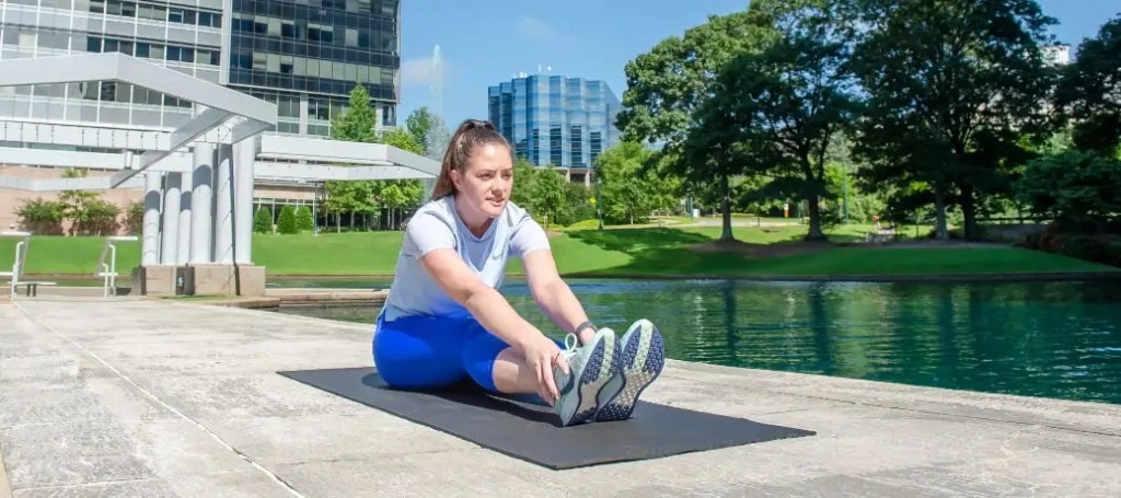 A woman stretching on a yoga mat in a quiet space outside an office building.