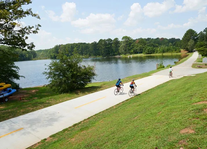 Group of people riding their bikes down a scenic bike path by a lake