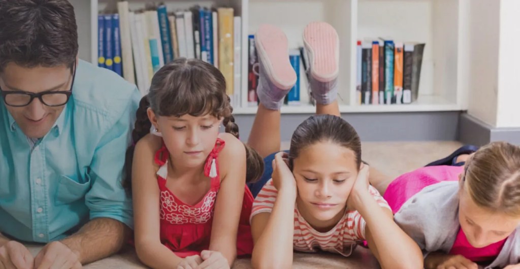 Three young girls laying down reading a book together