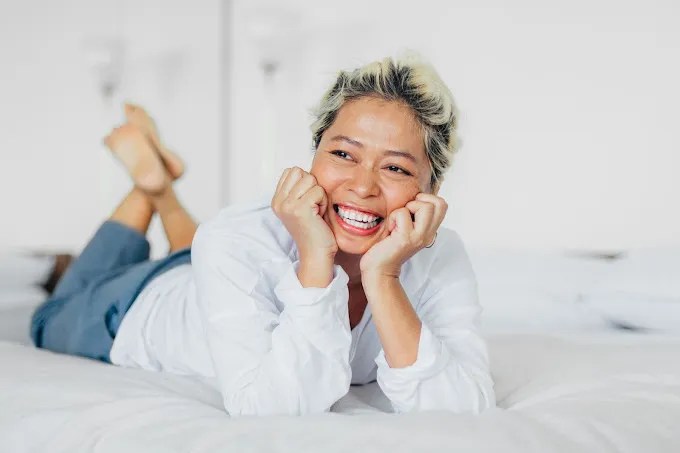 A woman lying on her bed, smiling.